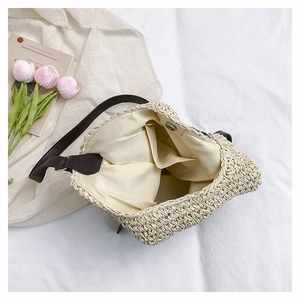 Detail view of woven straw bag interior with light beige lining and dark brown strap