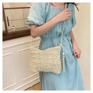 Detail of cream woven crossbody bag with wave texture and tassel charm on a model