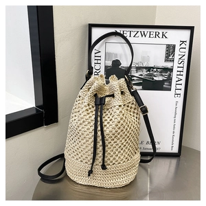 Détail d'un sac seau en paille tissée avec cordon en cuir noir et accents dorés chic
