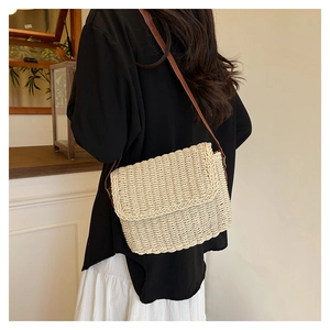 Dettaglio borsa in paglia beige intrecciata a mano con trama fine e tracolla in pelle