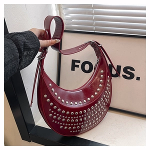 Detail view of red glossy patent leather hobo bag with silver metallic rivets and strap