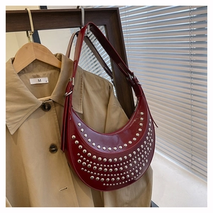 Detail of burgundy patent leather crescent bag featuring silver metallic studs and strap