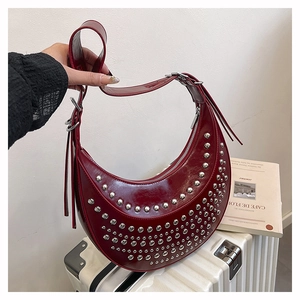 Close-up of a dark red crescent shoulder bag featuring silver rivets and polished finish
