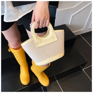 Detail view of woven shell bag featuring cream fabric and yellow leather handle