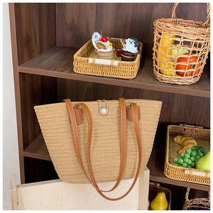 Detail of woven straw tote bag with brown leather straps and pearl button closure
