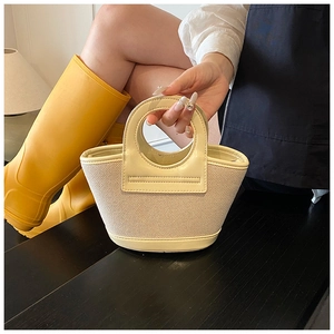 Detail of cream woven tote bag with round cutout handle and smooth leather trim