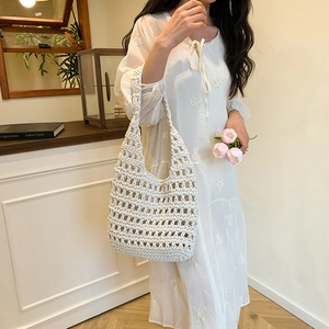 White crochet woven shoulder bag with hollow design held by a model in a floral dress