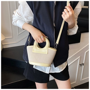 Detail of light yellow woven shell bag with round leather handles and silver hardware