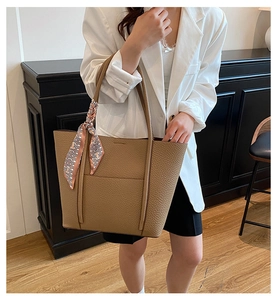 Detail of khaki leather tote bag with silk scarf on handle worn by woman in white blazer
