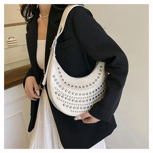 White crescent moon shoulder bag with silver rivet studs worn by a model in a cafe