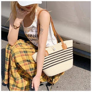 Detail of woven straw tote bag featuring black stripes and elegant faux pearl clasp