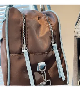 Detail of smooth metal double zippers on coffee nylon tote with light blue leather trim