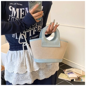 Detail of a beige woven shell tote bag with light blue patent leather handles and trim
