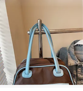 Close-up of contrast brown travel bag with blue leather handles and metal zipper detail