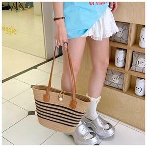 Detail of striped woven straw tote bag with brown leather handle and pearl clasp detail