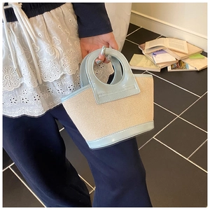 Detail of a chic woven shell handbag featuring light blue glossy leather handles and trim