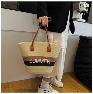 Close-up of a large striped straw tote bag with SUMMER text and leather handles