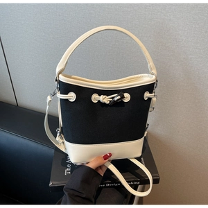 Detail of contrast canvas bucket bag featuring white PU leather trim and horn buckle closure