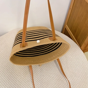 Detail of straw woven tote bag with black stripes, leather straps and pearl button closure