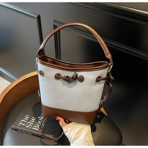 Detail of canvas bucket bag featuring dark brown leather trim and wooden horn button