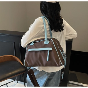 Detail of a large brown nylon travel bag with light blue leather trim and wide shoulder strap