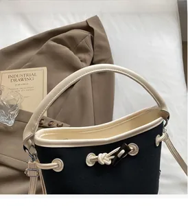 Detailed view of canvas bucket bag featuring contrast leather trim and knot buckle closure