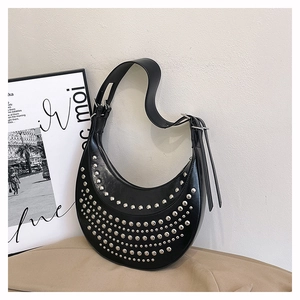 Black crescent shoulder bag with silver rivets and wide strap in home setting