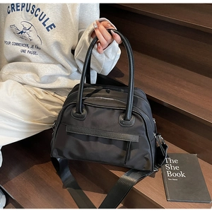 Detail of black nylon tote bag with leather trim and dual zippers on wooden steps
