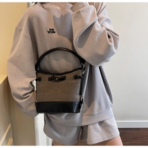 Detail of canvas bucket bag with black leather trim and horn toggle closure in a lifestyle setting