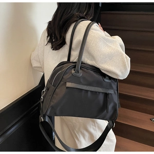 Detail of black nylon tote bag showing leather handles and wide detachable shoulder strap
