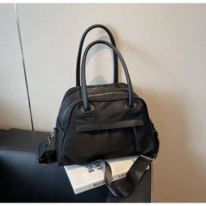 Detail of durable black nylon tote bag featuring leather handles and adjustable strap