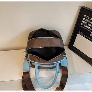 Detail view of the brown nylon tote bag with blue leather handles and dual zipper closure