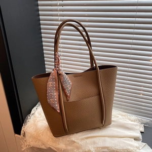 Brown pebbled leather tote bag with decorative geometric silk scarf on a white lace cloth