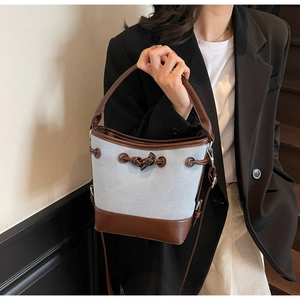 Detail of canvas bucket bag showing the drawstring closure and brown leather trim texture