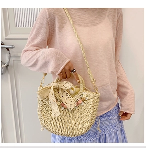 Detail of hand-woven straw bag featuring large lace bow and colorful floral accents