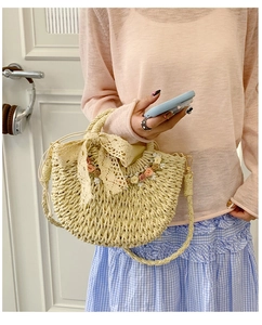 Detail of straw woven handbag featuring floral accents and white lace bow decoration
