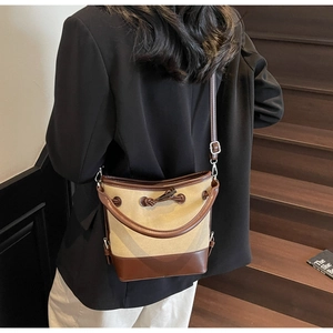 Close-up of canvas and leather bucket bag with drawstring on a brown wooden staircase