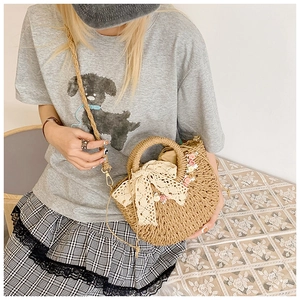 Detail of half-moon straw bag featuring white lace bow and delicate floral accents