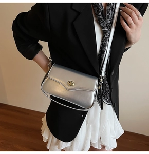 Détail du sac bandoulière argenté avec fermoir doré sur costume noir et jupe blanche