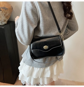 Détail du sac bandoulière noir avec fermoir doré rotatif porté par un mannequin