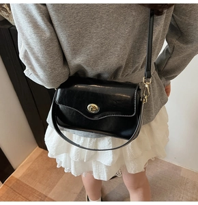 Détail du sac bandoulière en cuir noir avec élégant fermoir rotatif doré cylindrique