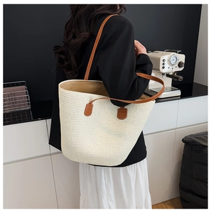 Detail of a large cream woven tote bag with brown leather straps on a model's shoulder