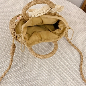 Detail of woven straw bag showing fabric lining, drawstring closure and lace bow