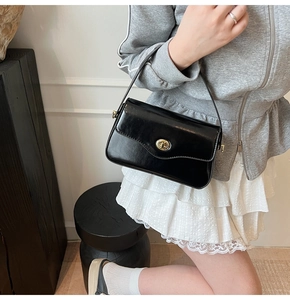 Détail du sac sous l'aisselle en cuir noir brillant avec fermoir rotatif doré et bandoulière
