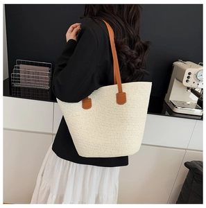 Detail of woven straw tote bag featuring brown faux leather straps and large capacity