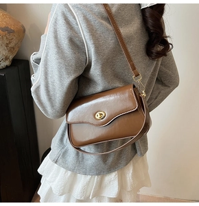 Détail d'un sac bandoulière en cuir marron avec un fermoir doré rond et une texture lisse