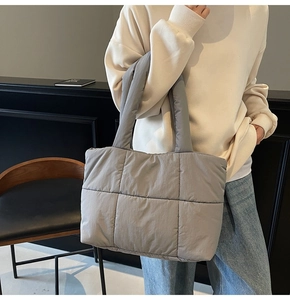 Close-up of grey quilted velvet tote bag carried by a model in a minimalist indoor setting