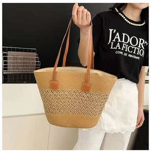Detail of a large woven straw tote bag with brown leather handles and dual-tone stitching