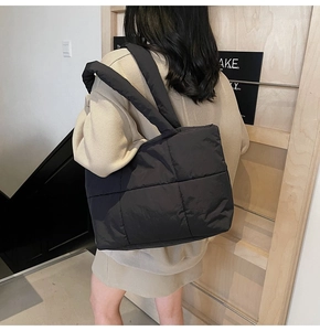 Close-up of black quilted down tote bag with wide shoulder strap worn by a model