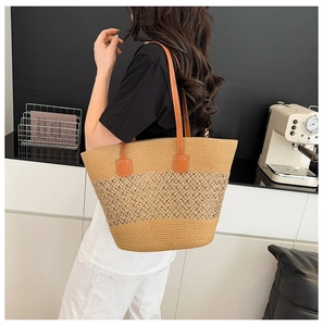 Detail of a large woven straw tote bag with brown leather handles in a home setting